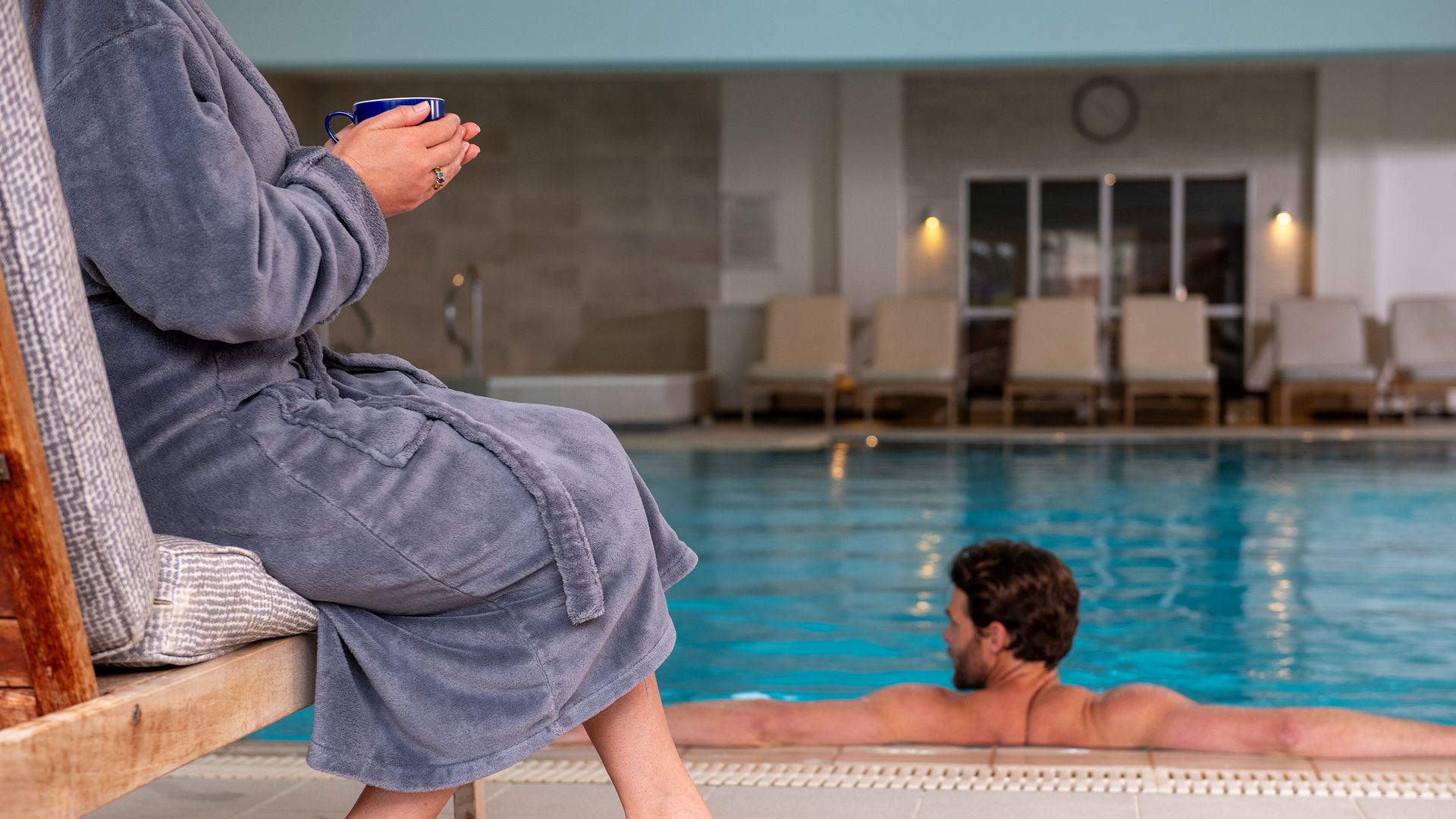 Man in spa pool, woman to the left with a warm drink in hand