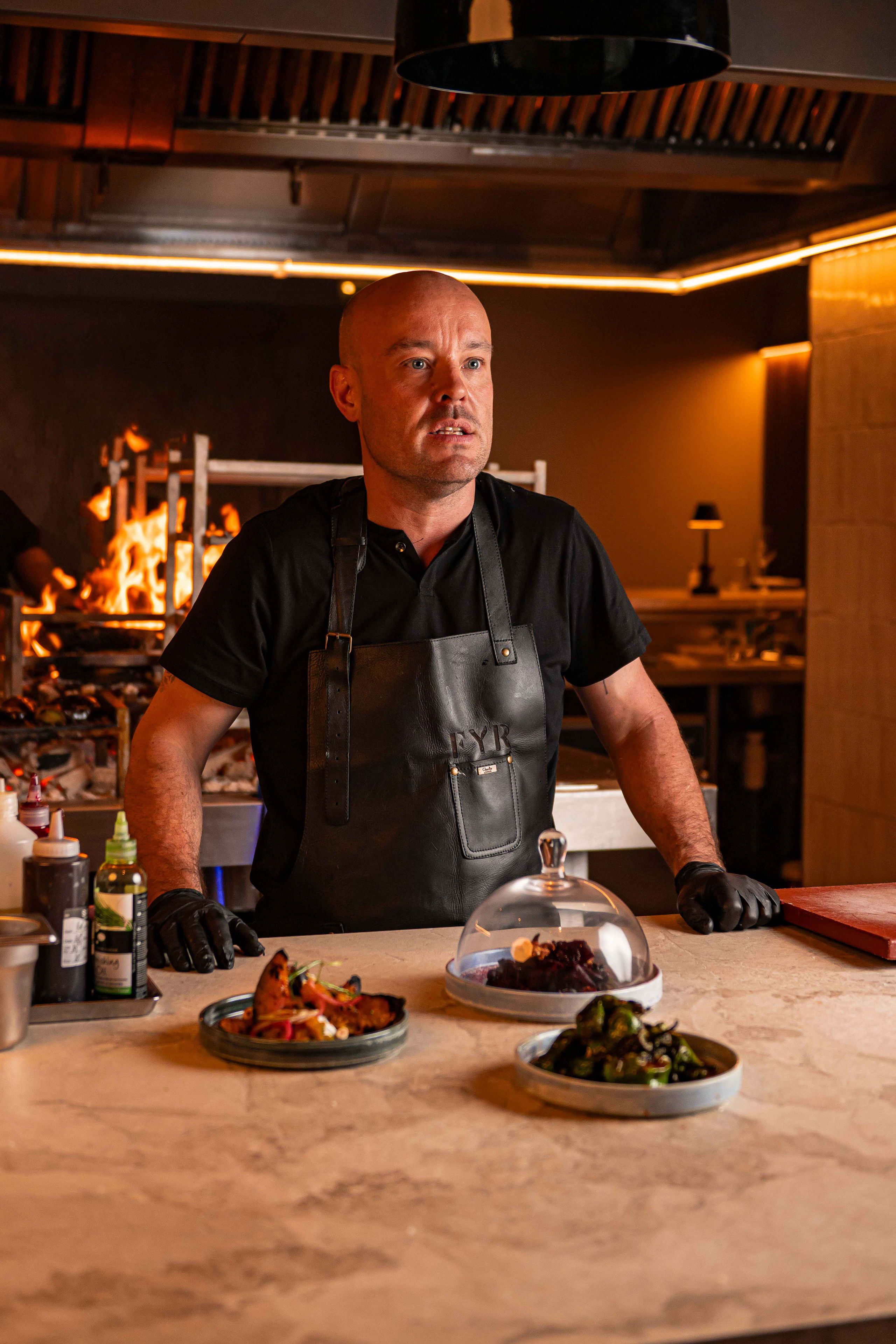 chef standing at a kitchen pass counter waiting to send out the food from FYR grill